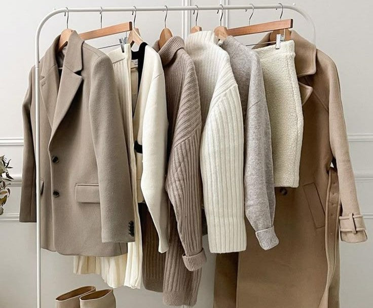 The image shows various coats for women in shades beige on a steel frame clothing rack. The coats are aesthetically placed one after the other interspersed with a sweater, skirt, cardigan that would all go with these coats