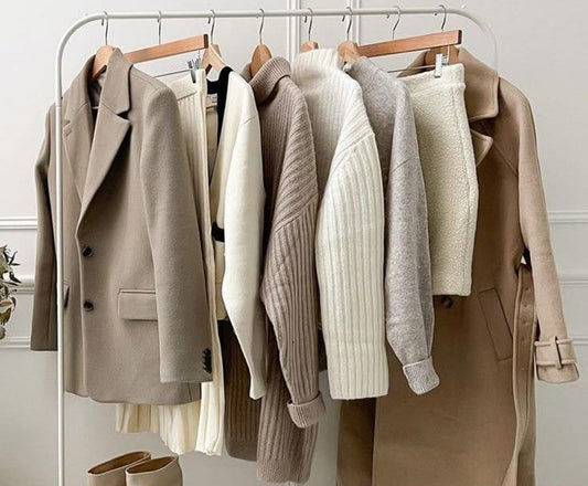The image shows various coats for women in shades beige on a steel frame clothing rack. The coats are aesthetically placed one after the other interspersed with a sweater, skirt, cardigan that would all go with these coats