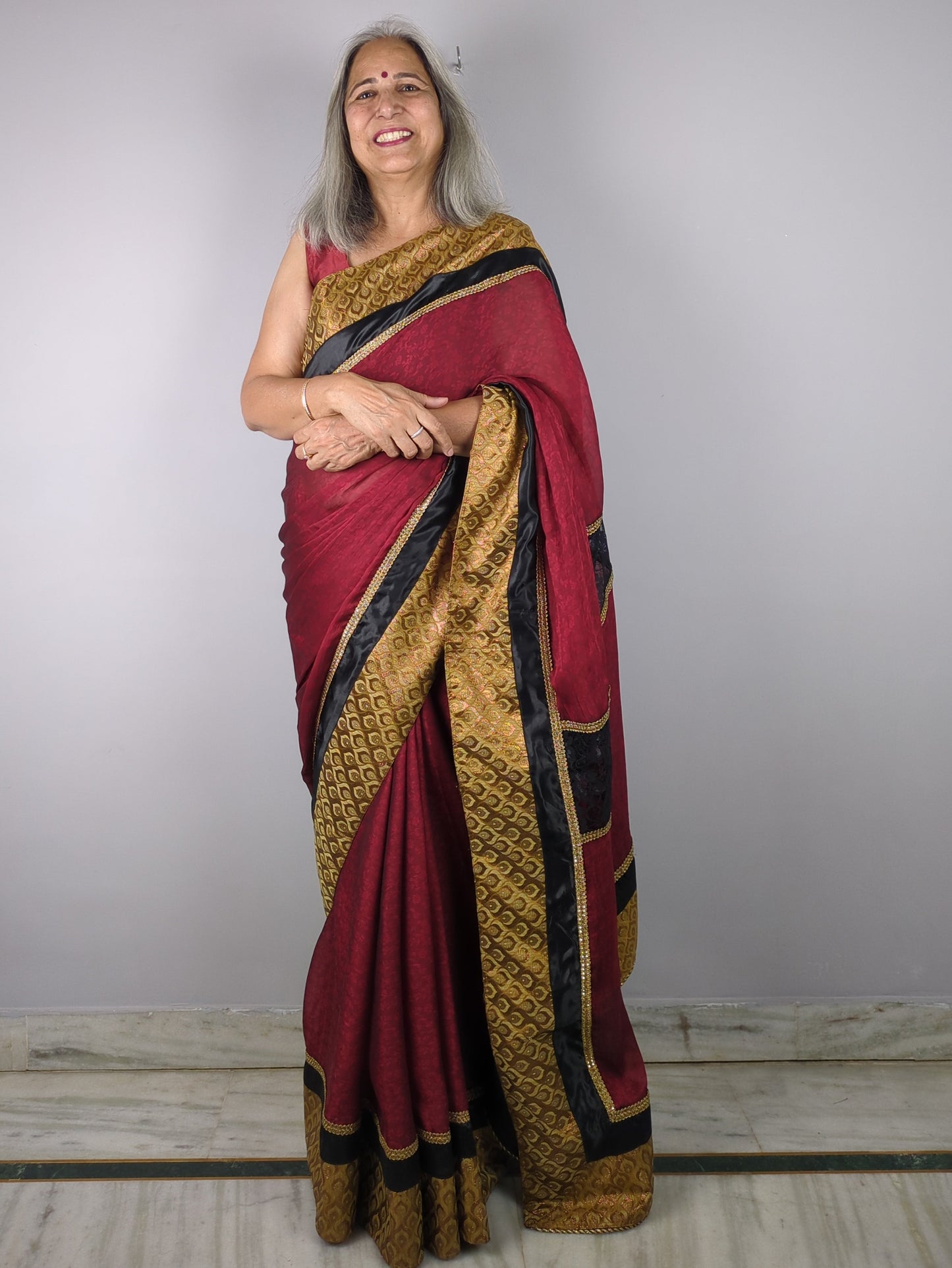 Woman wearing a red and gold saree against a plain background