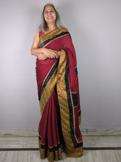 Woman wearing a red and gold saree against a plain background