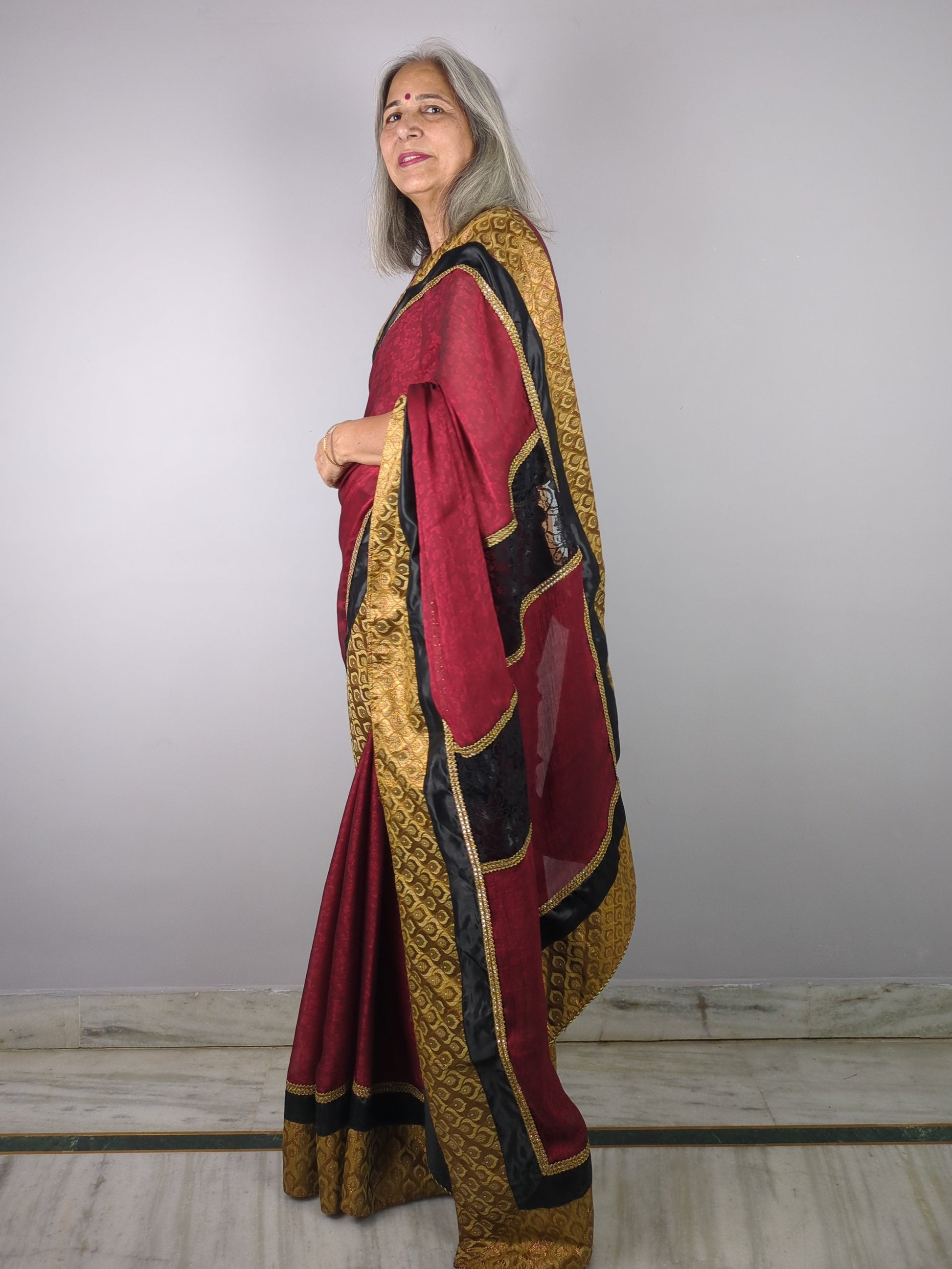 Woman wearing a traditional outfit with red, gold, and black colors on a plain background