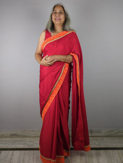 Woman wearing a red saree with orange border against a plain background