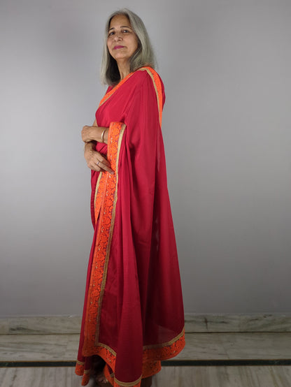 Woman wearing a red saree with orange border against a plain background