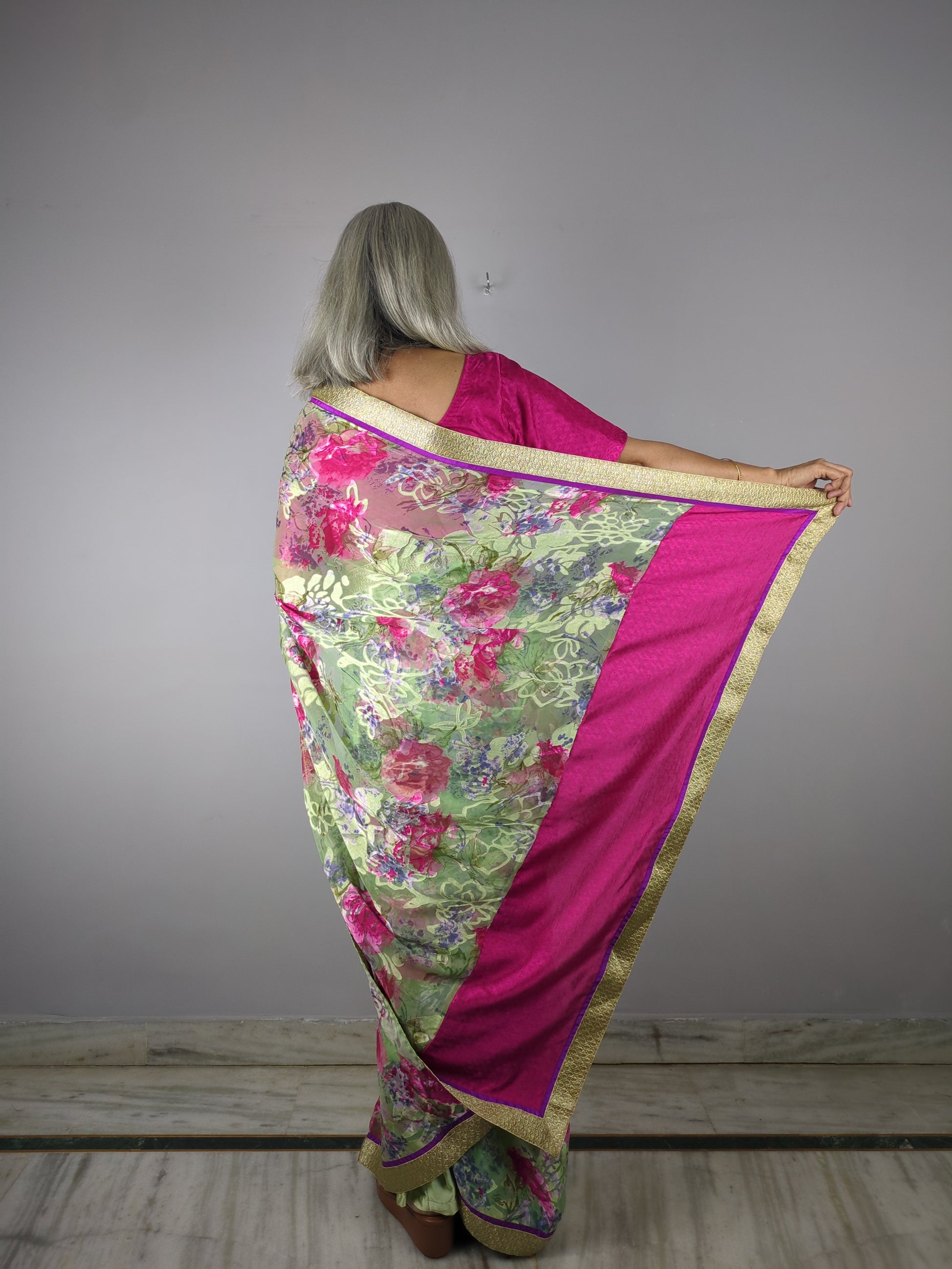 Person holding a pink and green floral saree against a plain background