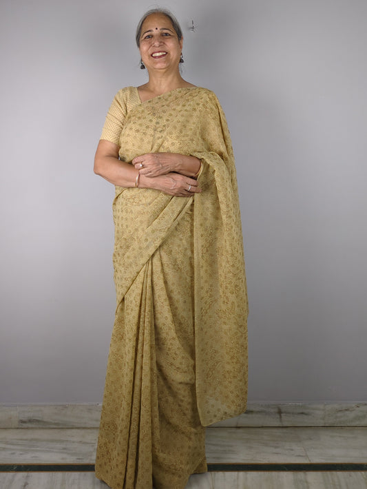 Person wearing a gold saree standing against a plain background