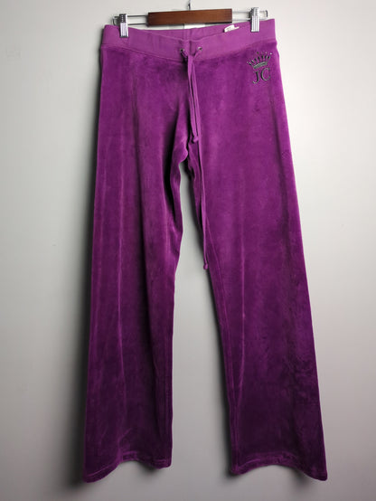 Purple velvet lounge pants hanging on a wooden hanger against a plain light gray wall.