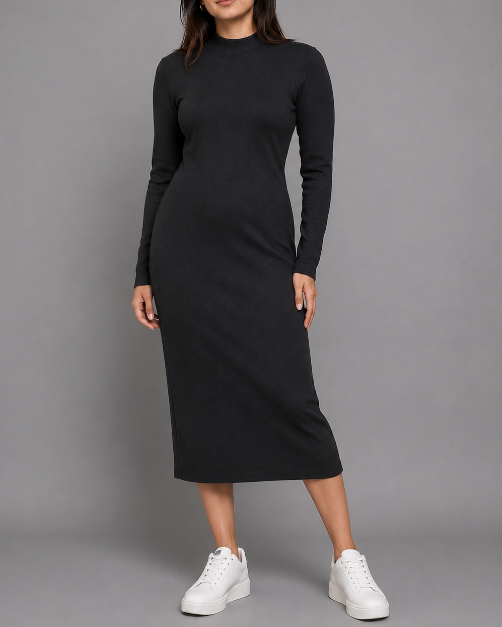 A woman modeling a black long-sleeve mock neck midi dress with white sneakers, standing against a solid gray studio background.