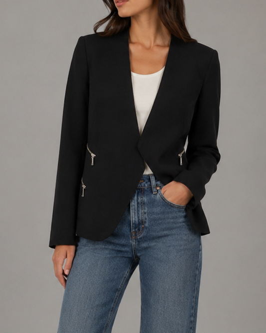 Person wearing a black blazer, white top, and blue jeans on a gray background