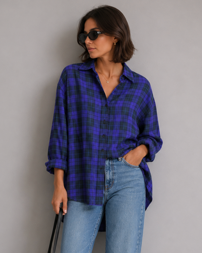 Woman wearing a blue plaid shirt and jeans, holding a black bag against a gray background