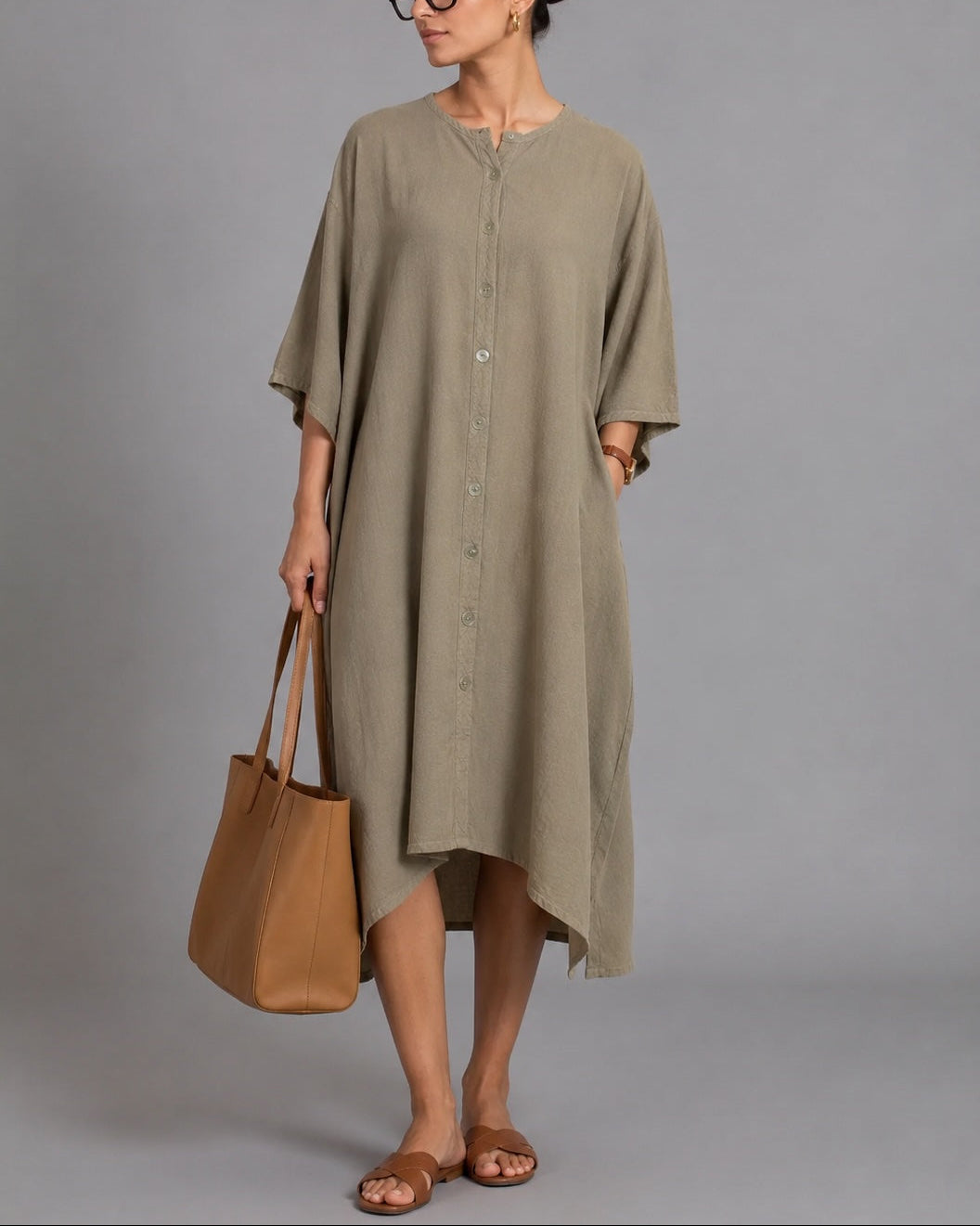 Woman wearing a long olive green dress holding a brown bag against a gray background