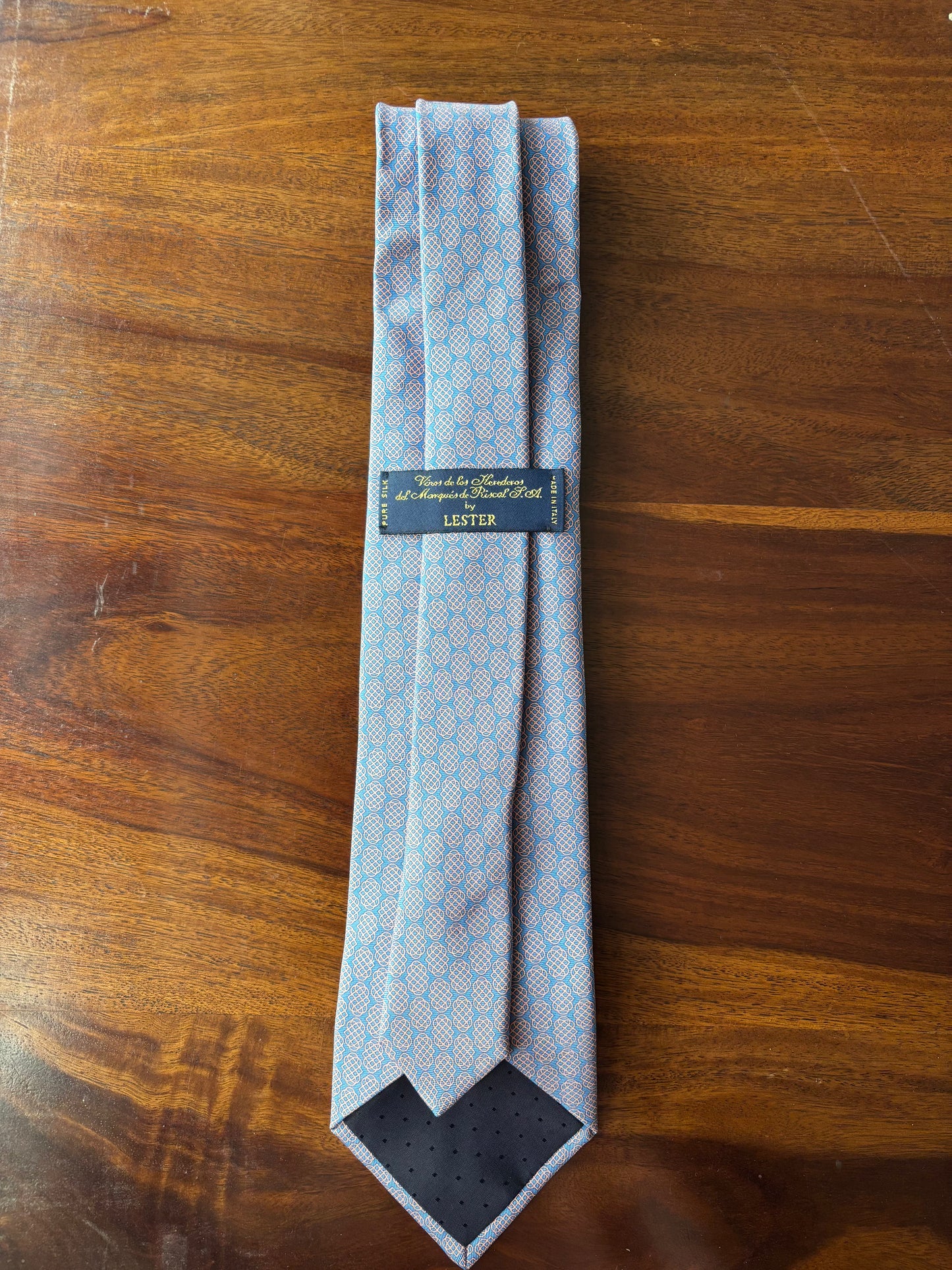 Folded blue patterned tie with a brand label on a wooden surface