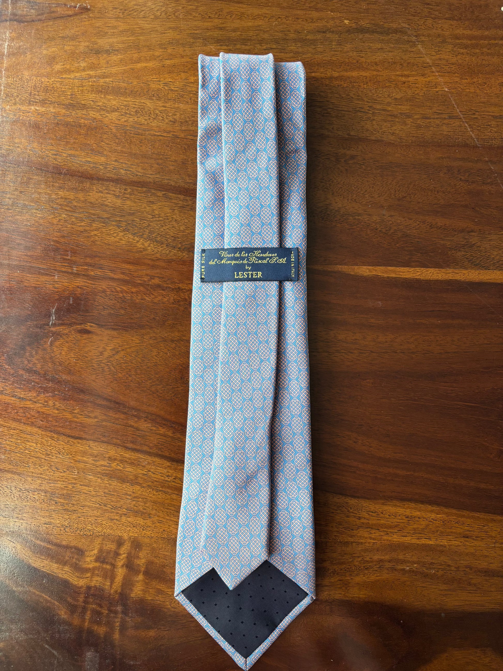 Folded blue patterned tie with a brand label on a wooden surface
