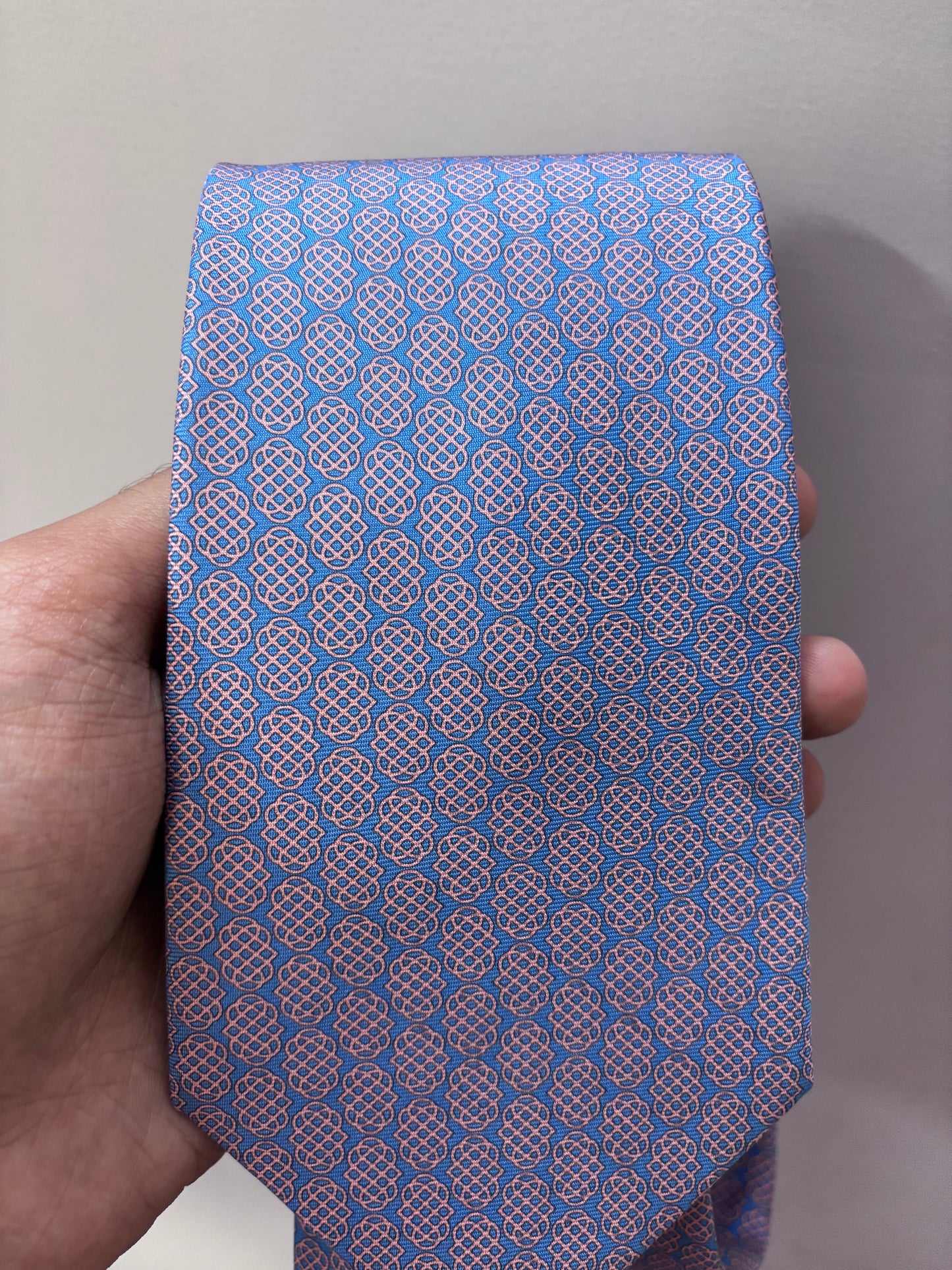 Blue tie with a geometric pattern held by a hand against a neutral background