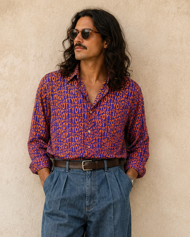 Man wearing a patterned shirt and blue jeans against a beige wall