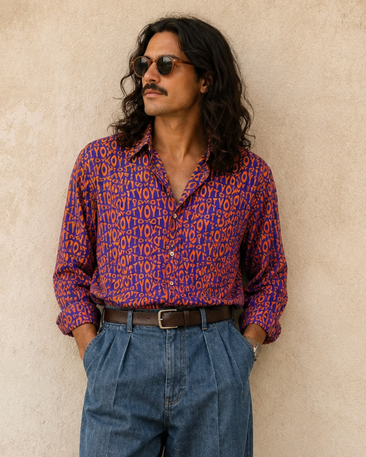 Man wearing a patterned shirt and blue jeans against a beige wall