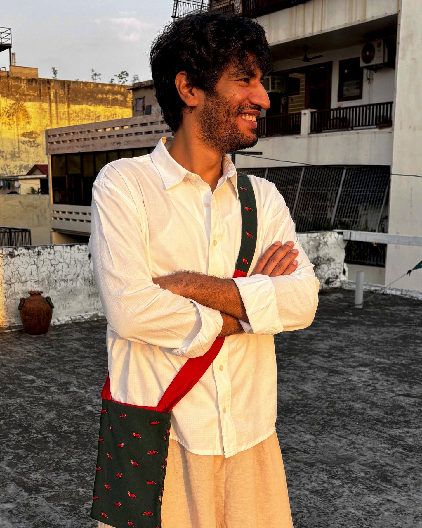 Man wearing a white shirt and beige pants with a green bag, standing on a rooftop.