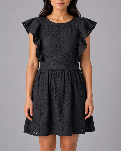 Woman wearing a black dress with ruffled sleeves against a gray background