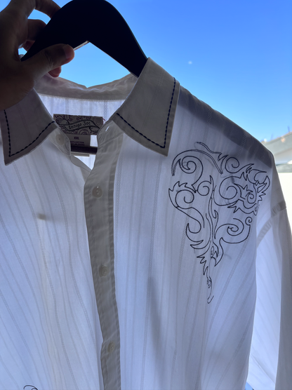 White shirt with black embroidery on a hanger against a blue sky.