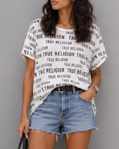 Woman wearing a True Religion t-shirt, denim shorts, and white sneakers on a gray background