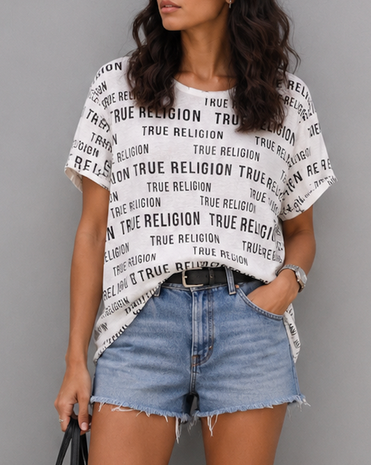 Woman wearing a True Religion t-shirt, denim shorts, and white sneakers on a gray background