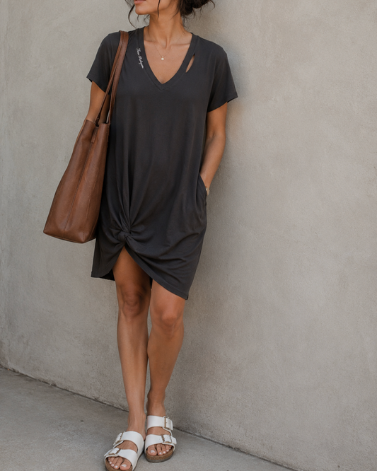 Woman in a black dress and cap standing against a plain wall